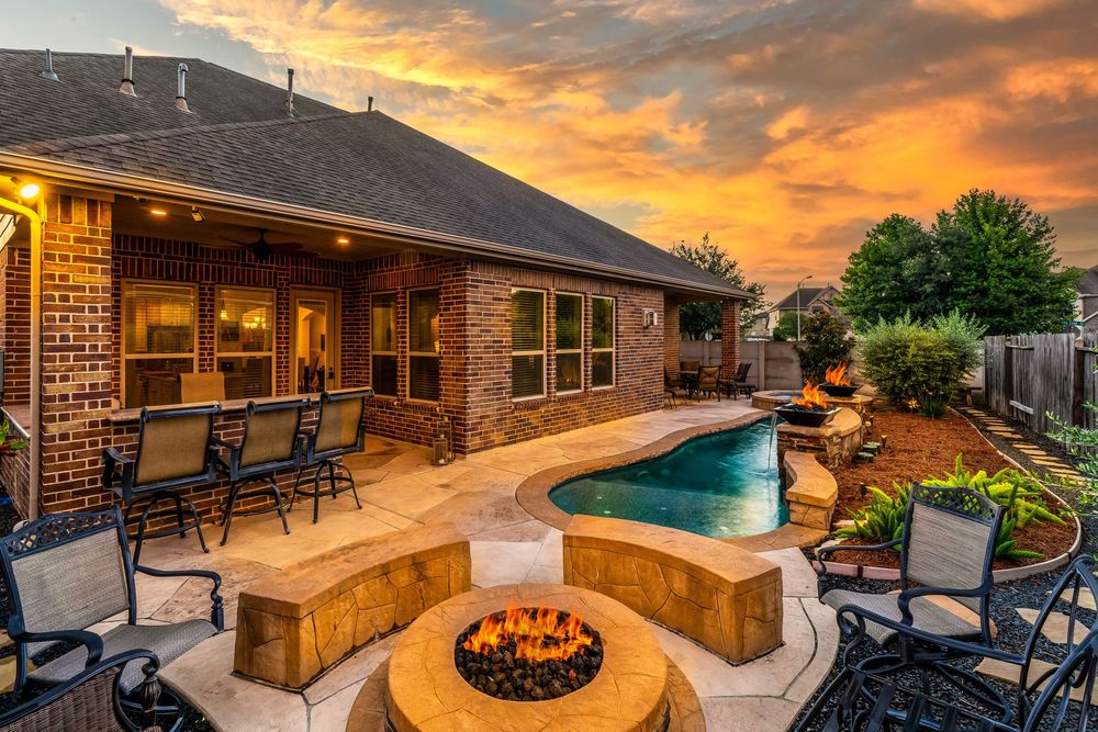 Luxurious backyard with pool, fire pit, and covered patio against a dramatic orange sunset sky.