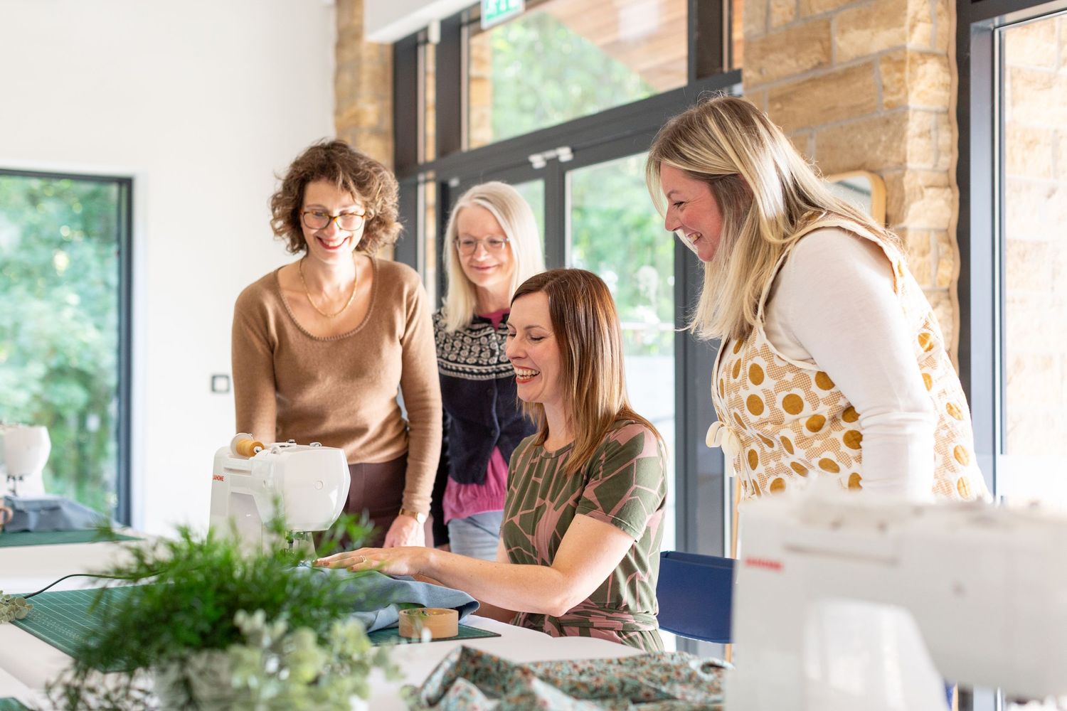 Group gathers around table for creative workshop with plants and crafting materials.