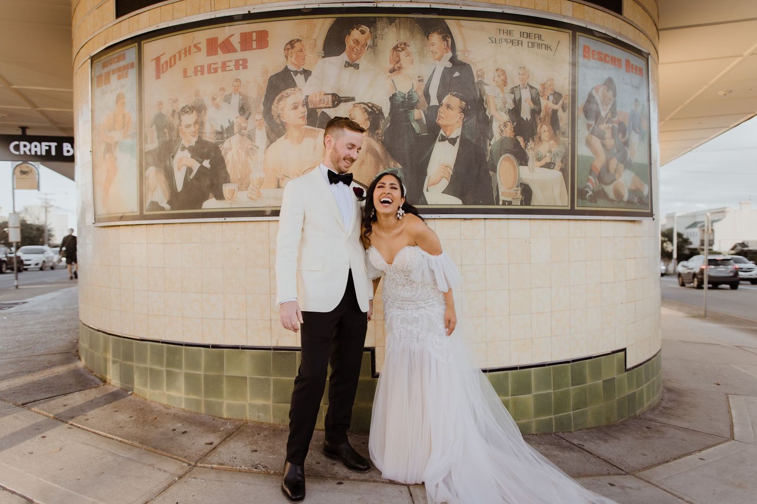 Bride and groom posing in front of vintage movie posters outside urban wedding venue at night.