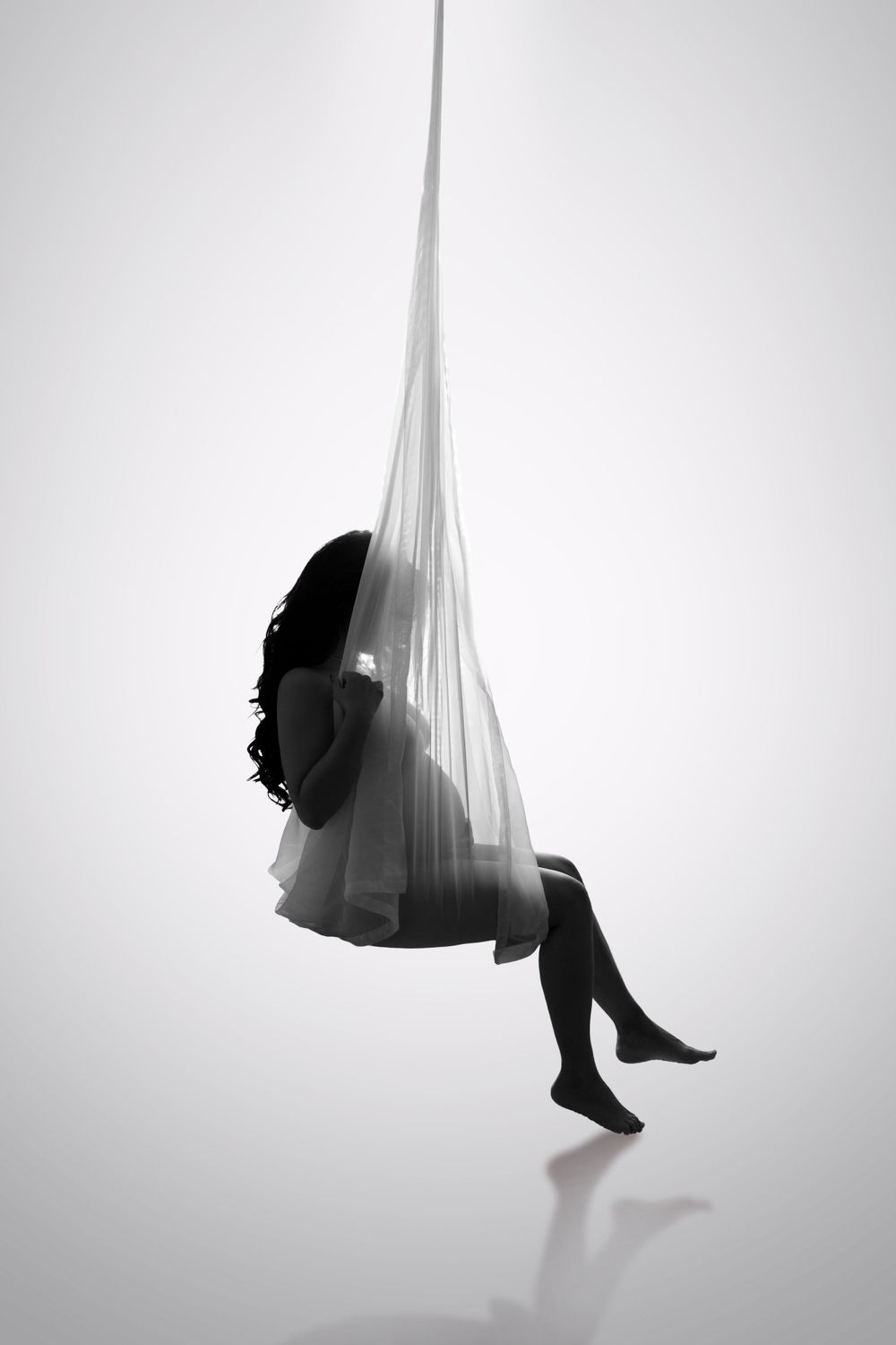 Artistic black and white portrait with flowing fabric creating suspended silhouette.