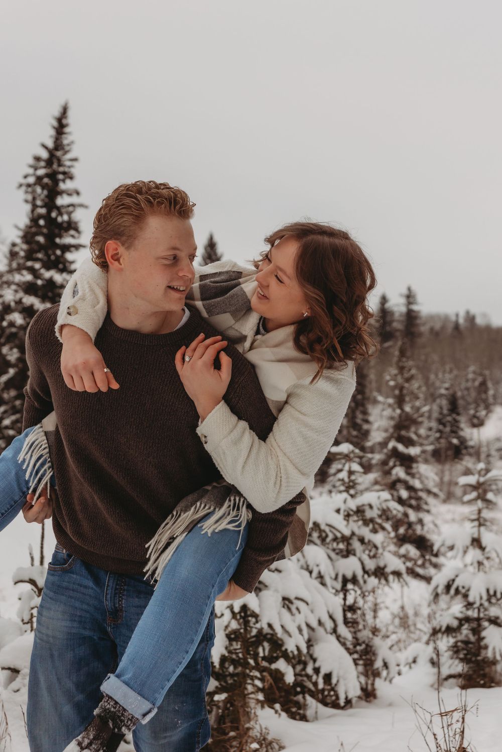 A playful winter piggyback ride moment against a snowy mountain backdrop.