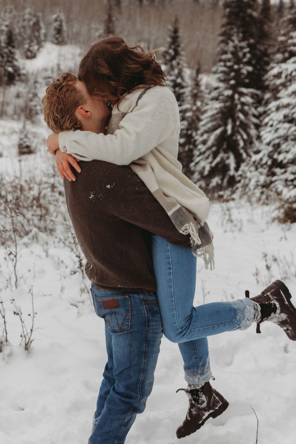 A joyful embrace in a snow-covered forest with evergreen trees in the background.