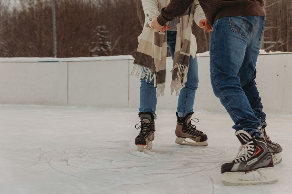 Close-up of ice skates on a frozen rink with two people skating together.
