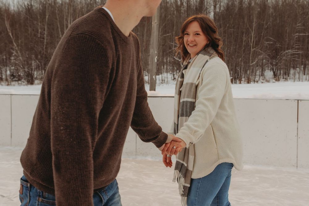 Two people ice skating together on a winter rink surrounded by snowy landscape.