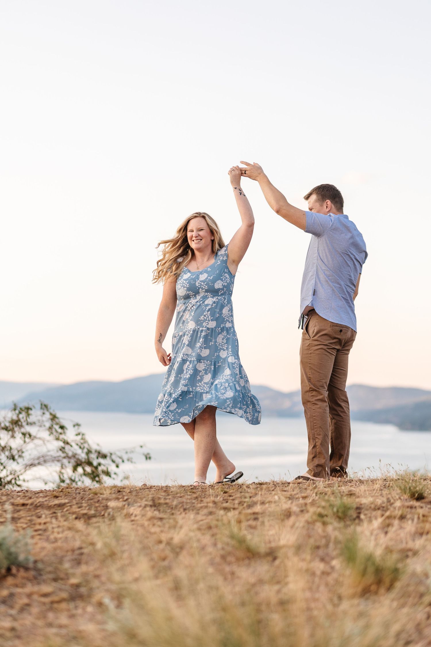 A couple dances joyfully on a hilltop during sunset.