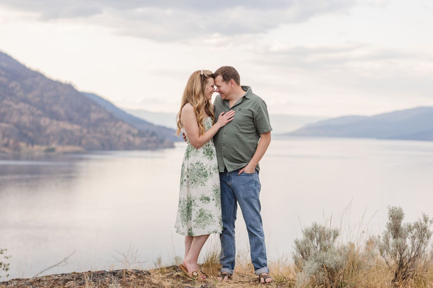 Couple embraces near a scenic mountain lake during a romantic photoshoot at sunset.