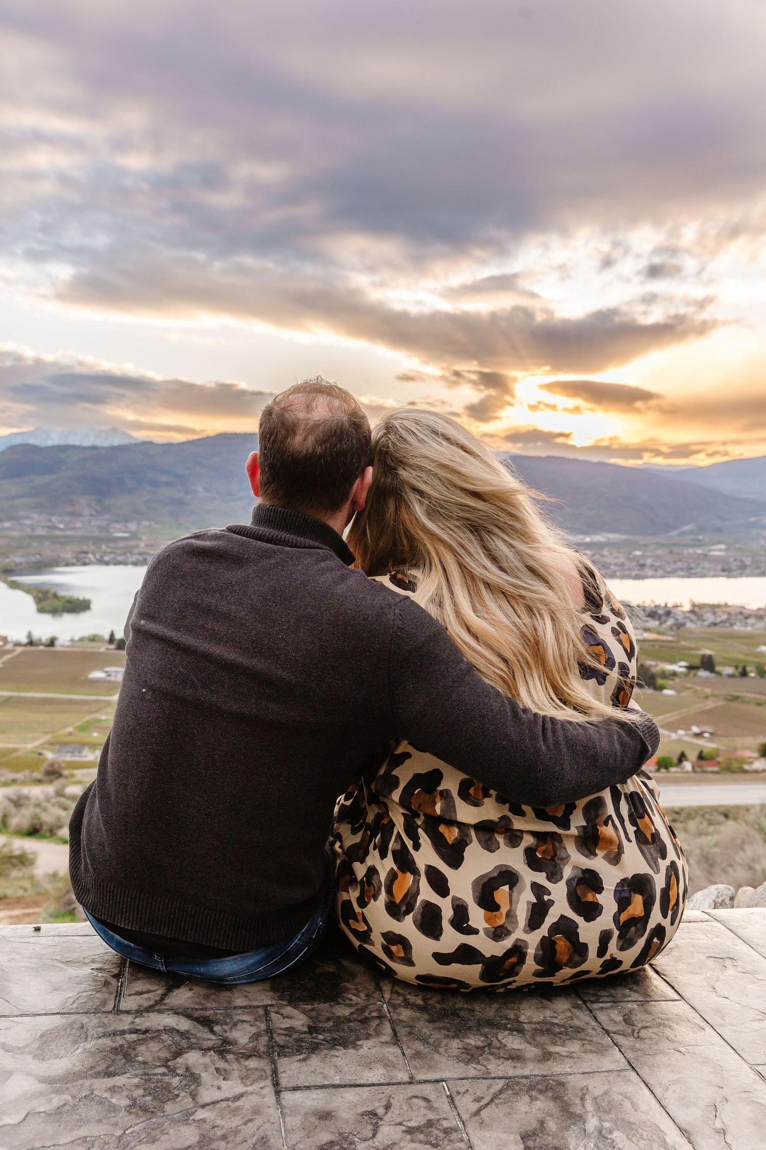 Couple cuddling while watching sunset over valley from scenic overlook.