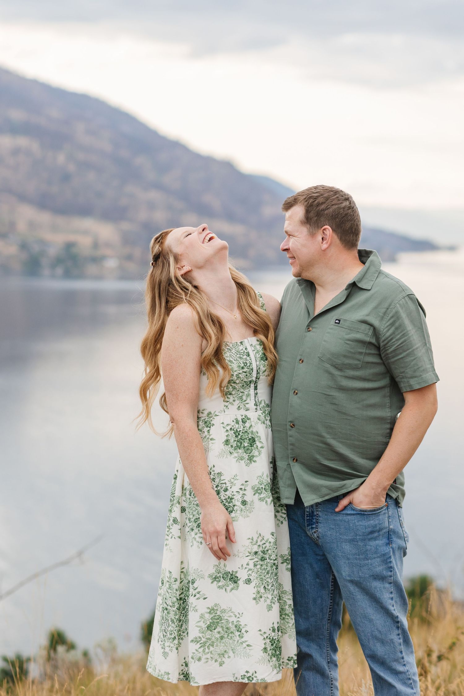 A couple shares joyful moments together during a photoshoot by a scenic mountain lake at sunset.