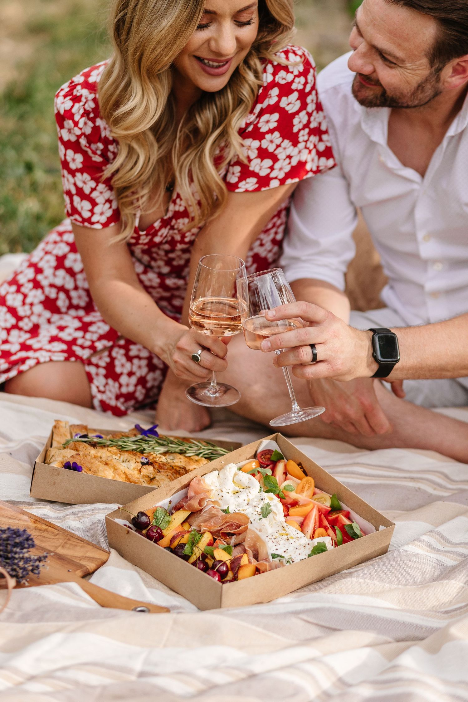 A couple shares takeout food and drinks during an outdoor picnic.
