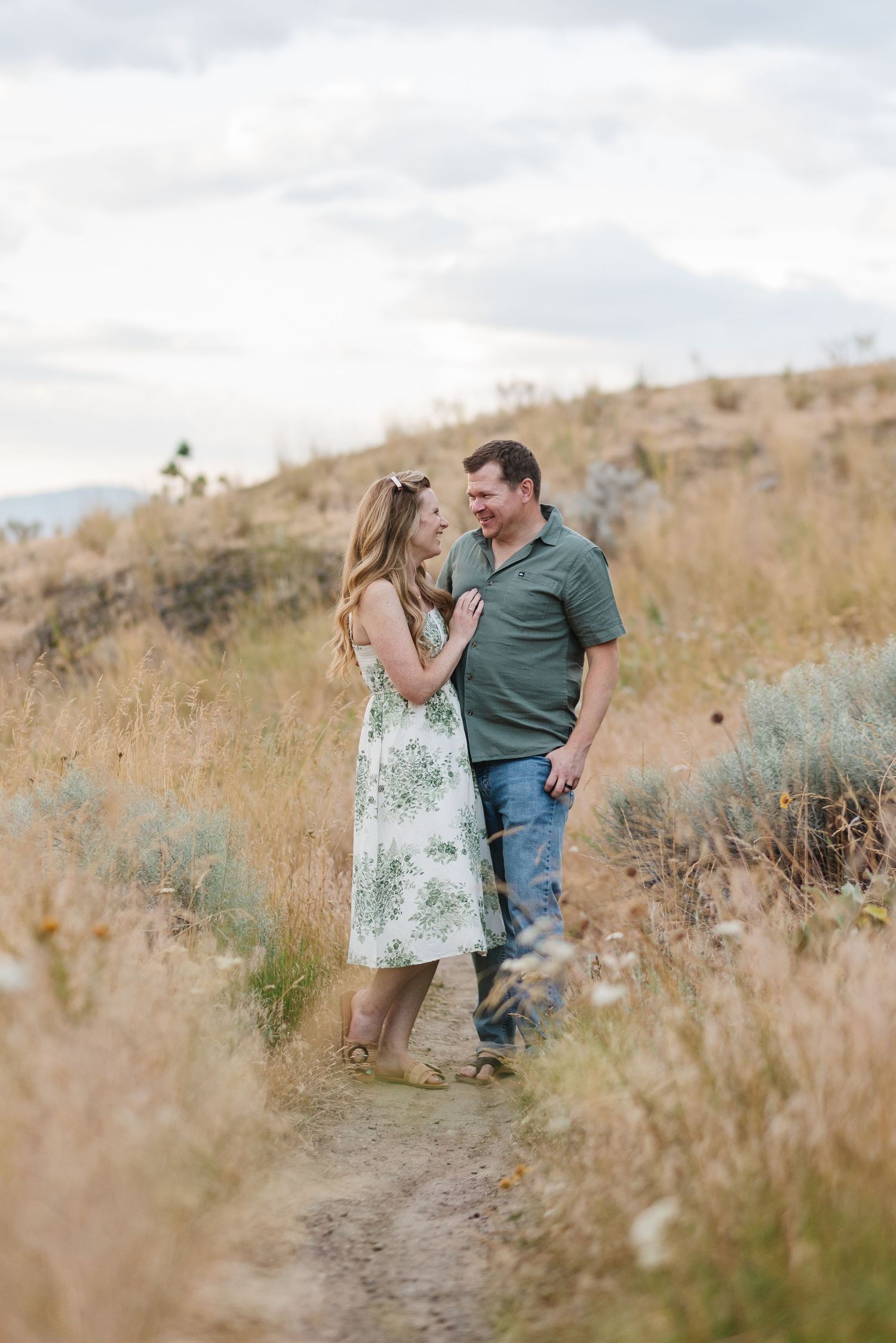 A couple shares a tender moment while standing together in a golden field of tall grass on a hillside.