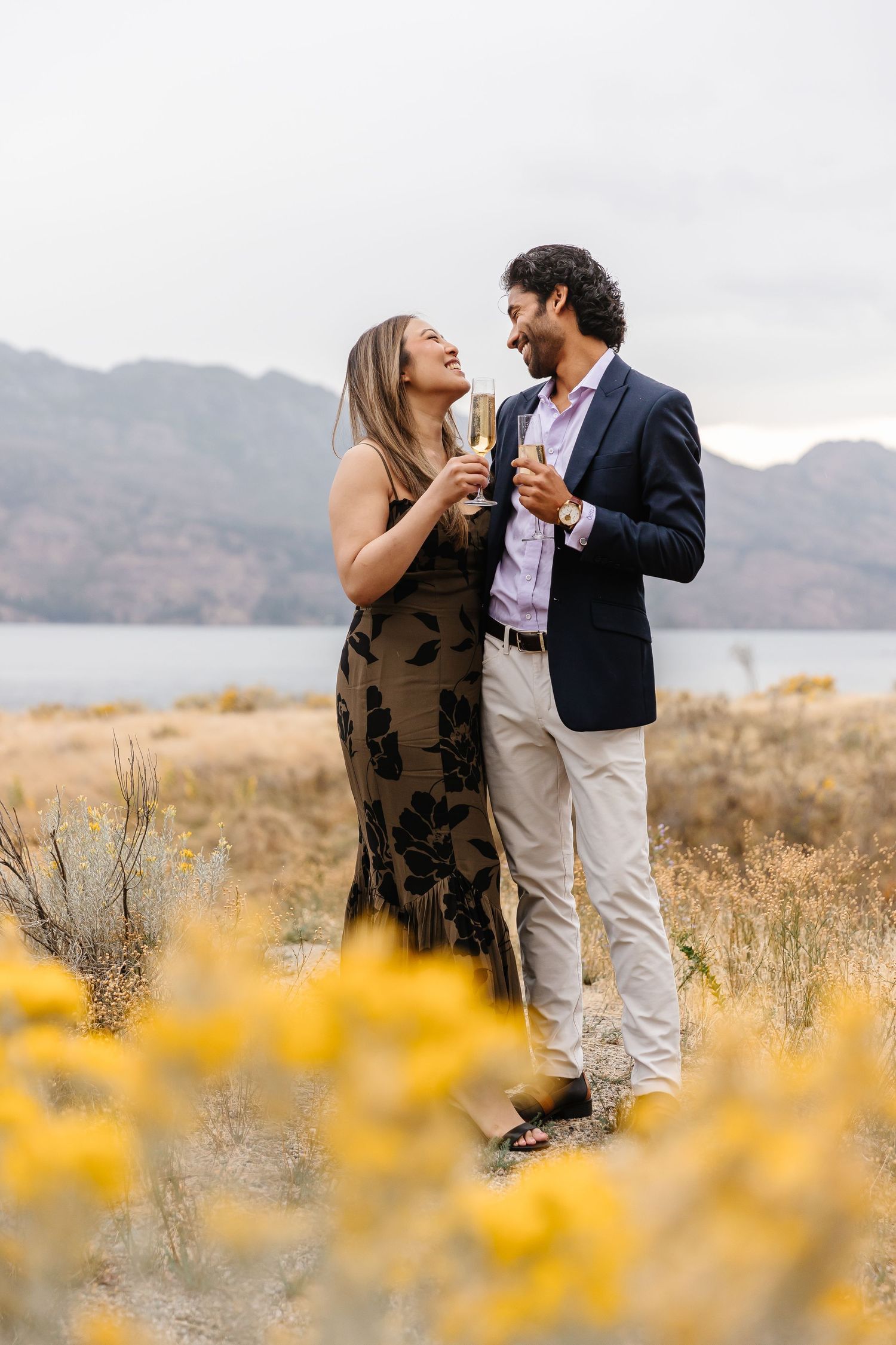 Couple shares romantic moment in field of yellow wildflowers with mountains in background.