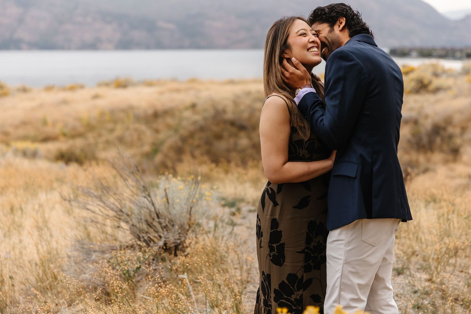 Intimate couple portrait in golden field with mountains and cloudy sky backdrop.