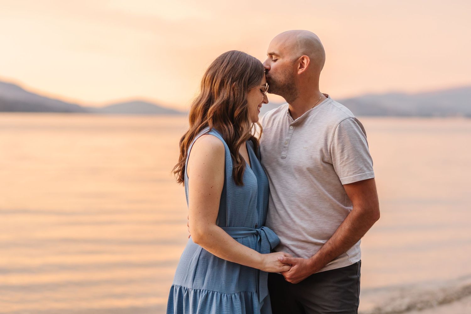 Couple sharing romantic moments during sunset at a beach with mountains in the background.