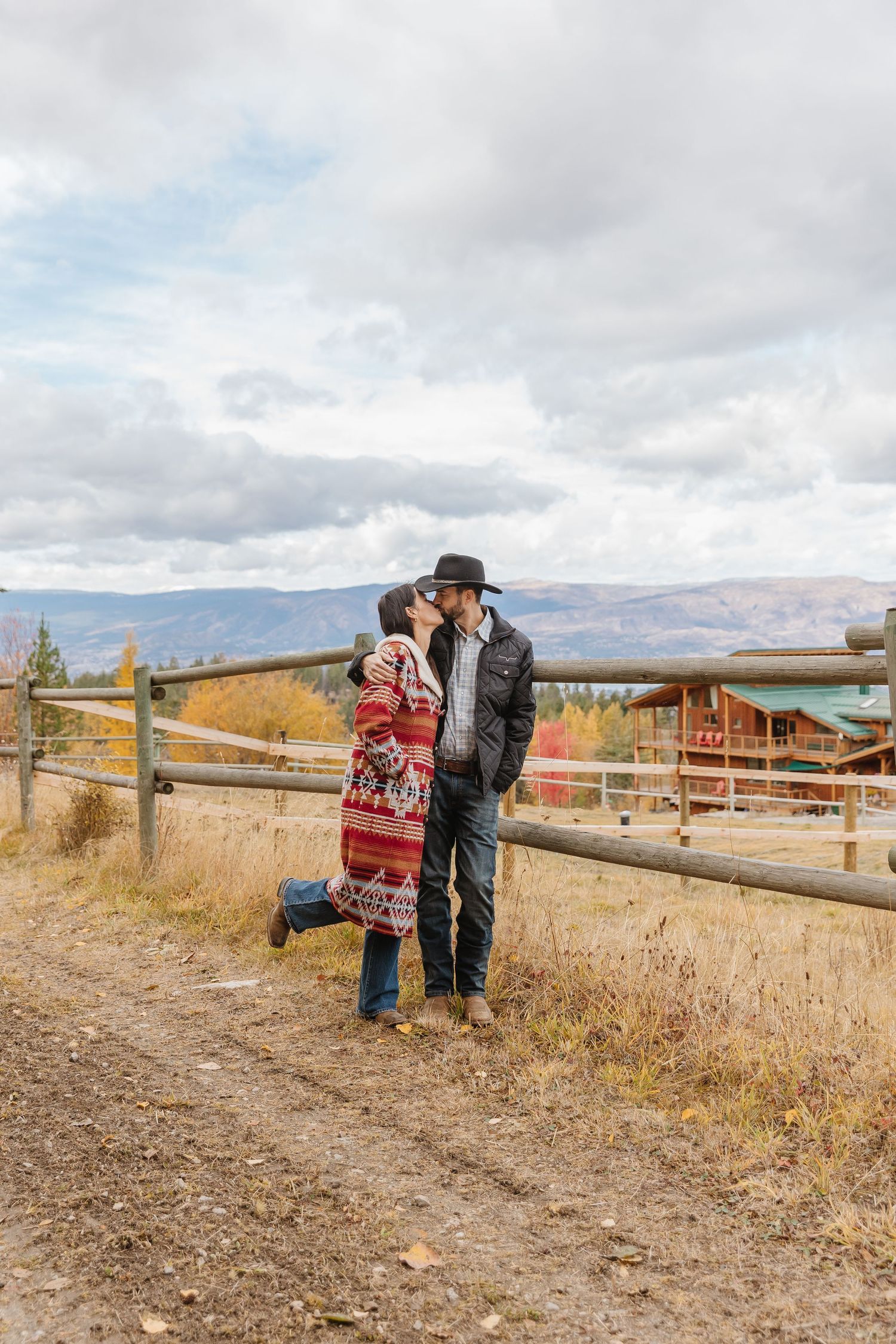 People enjoying a scenic view from a rustic wooden fence overlooking mountains and countryside on an autumn day.