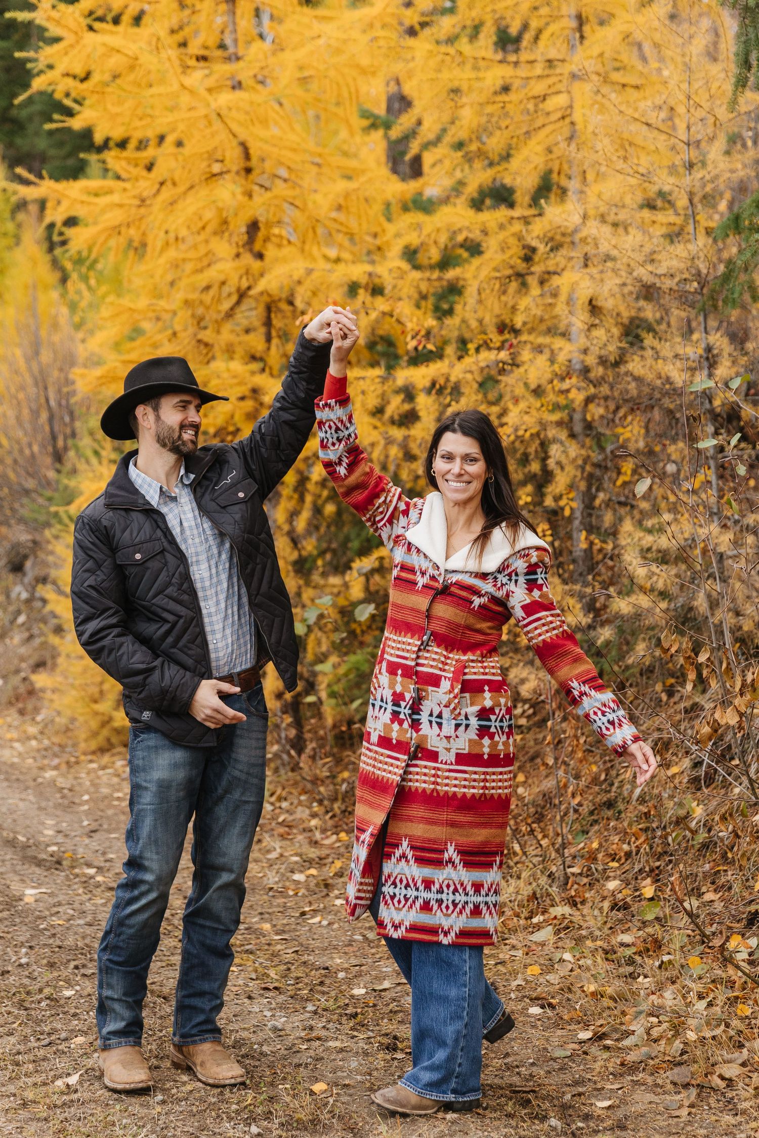 A couple in winter clothing shares playful moments against a backdrop of golden autumn foliage.