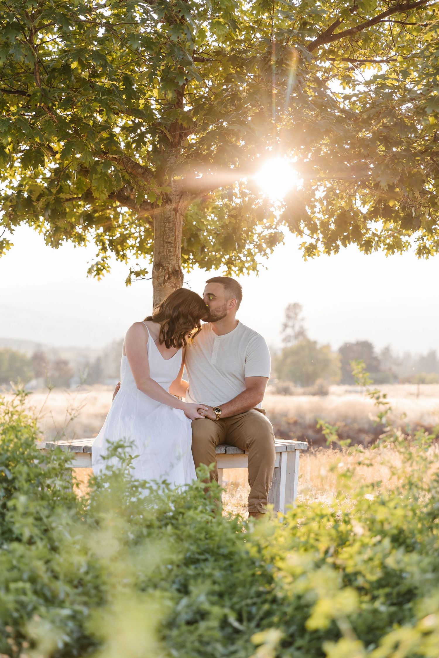 A couple shares a romantic moment at sunset in a lush garden setting with golden sunlight filtering through the trees.