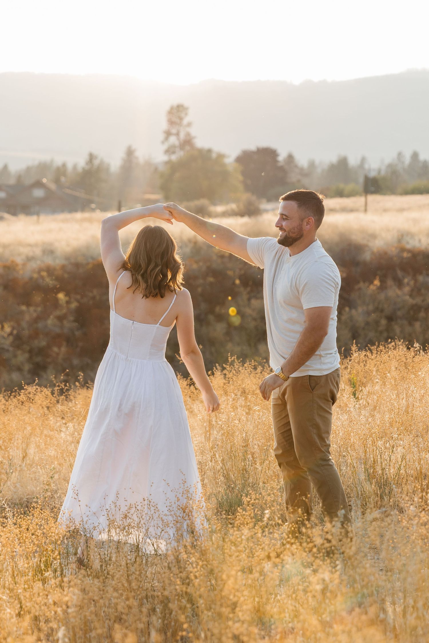 A couple dances together in a sun-drenched golden field during a romantic summer evening photoshoot.