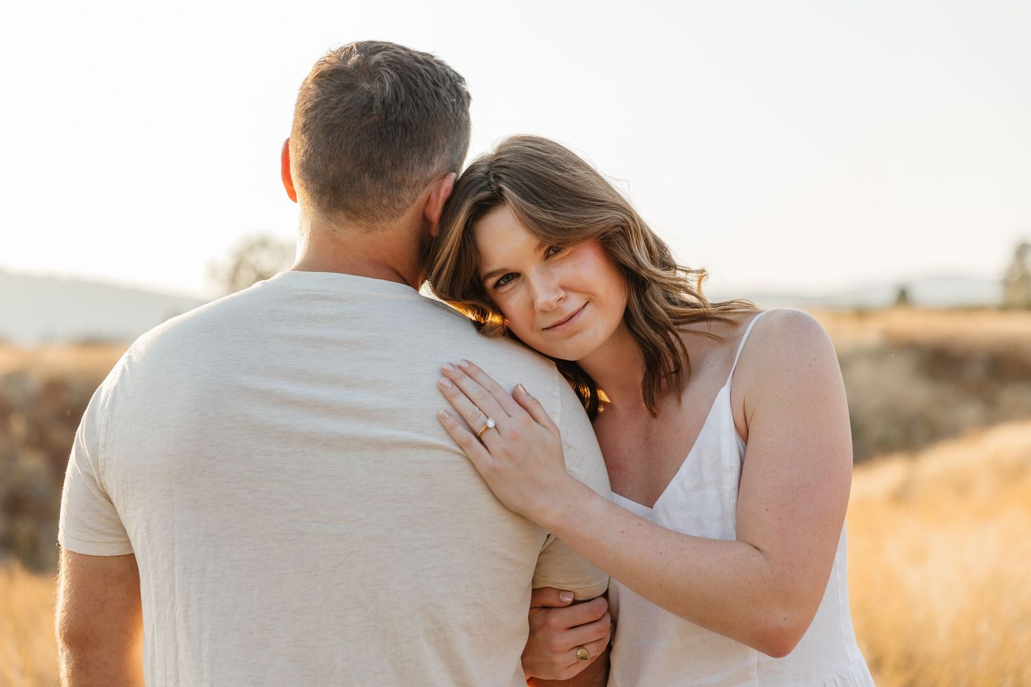 Romantic couple embraces in golden sunlit field during outdoor photo session.