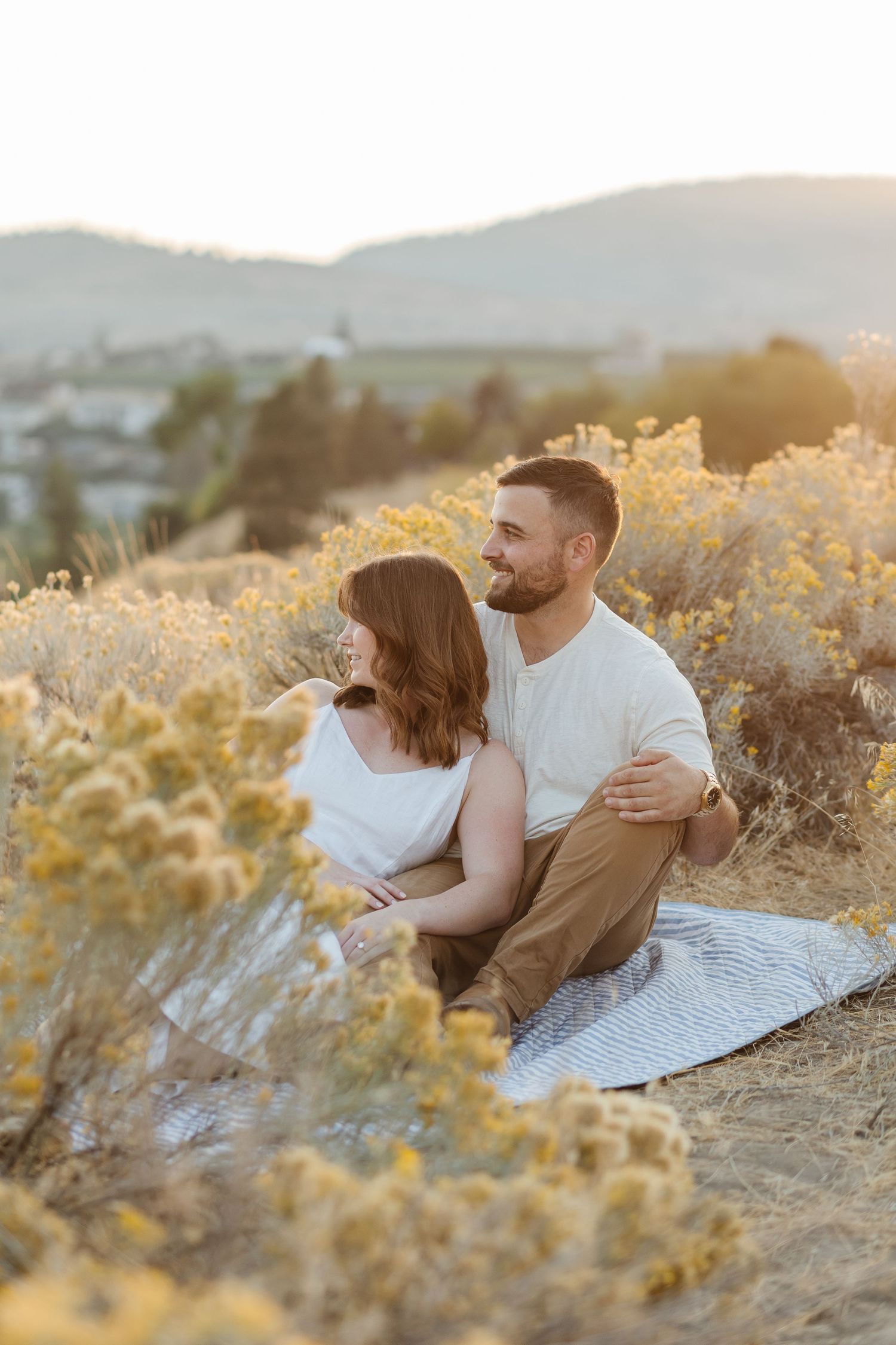 A couple shares a tender moment while sitting in a golden wildflower field at sunset.