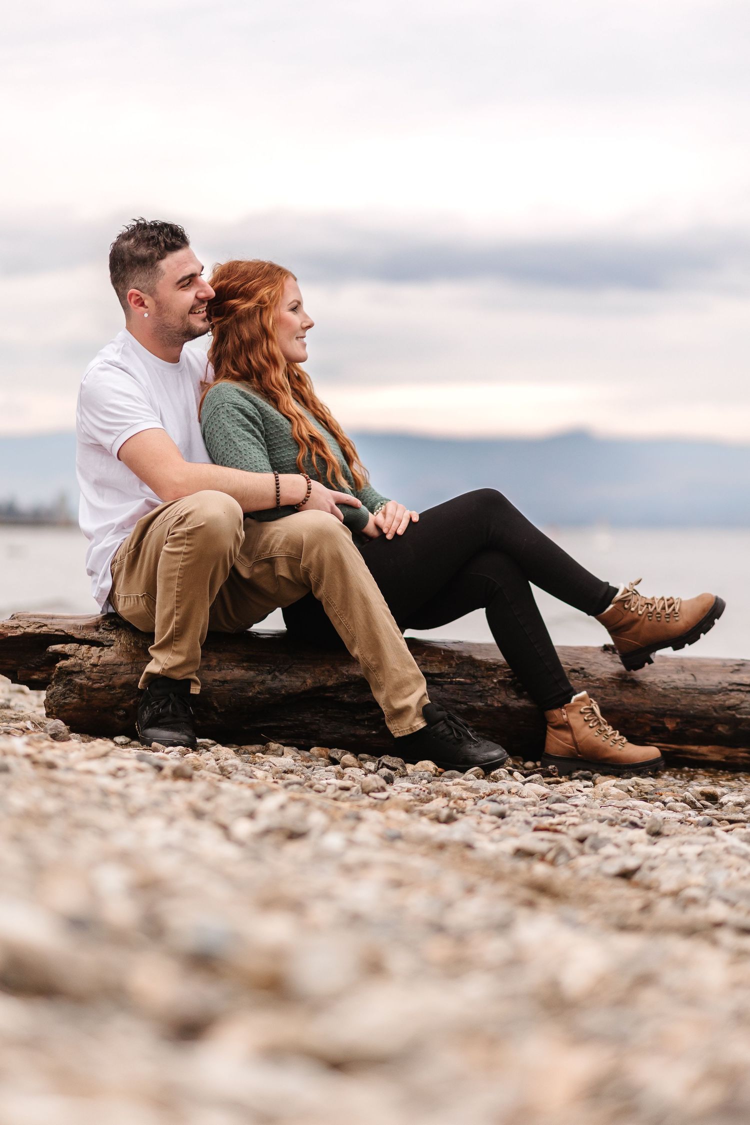 Couple relaxing on rocky beach shore during cloudy evening photoshoot.