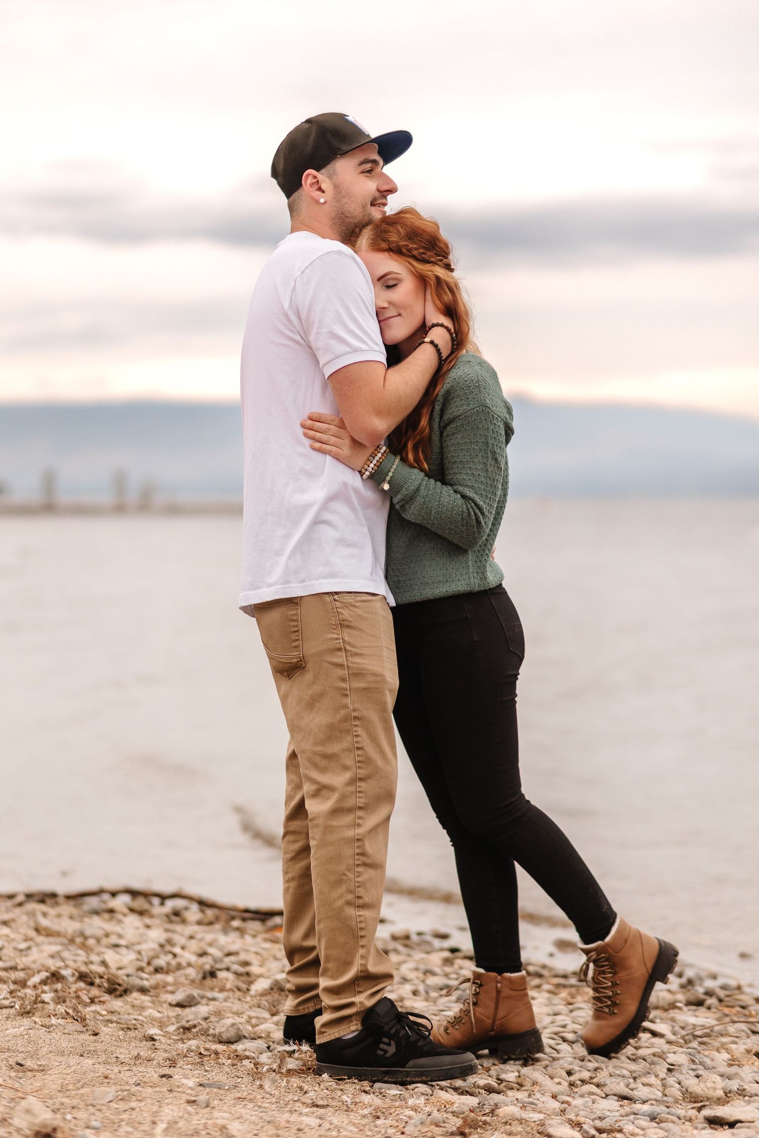 A romantic couple embraces on a rocky beach at sunset.