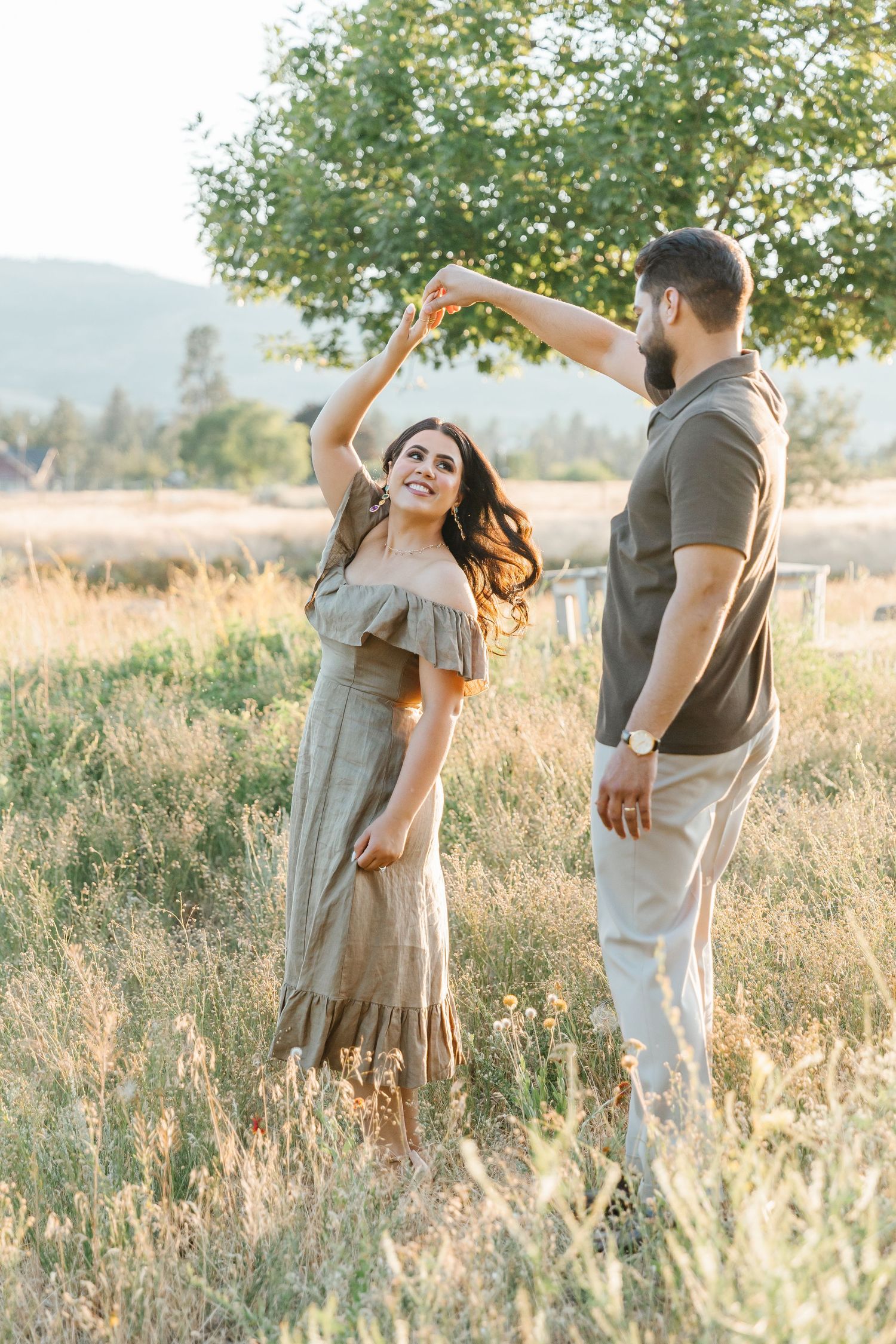 A couple shares a romantic moment in a sunlit meadow with tall grass and trees in the background.