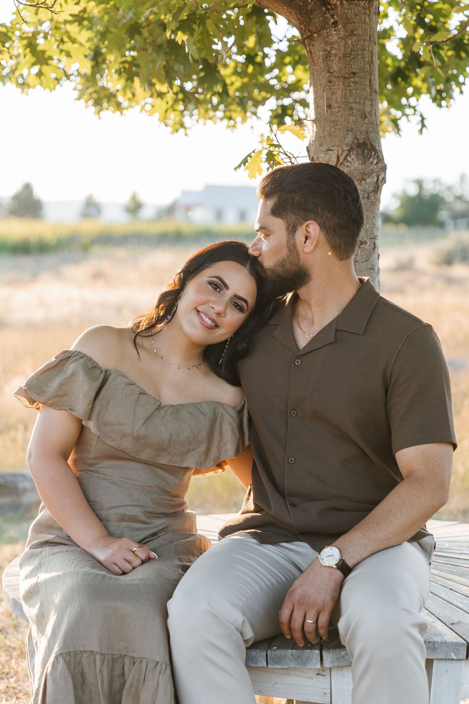 A couple shares tender moments while sitting on a bench in a sunlit outdoor setting during a photo session.