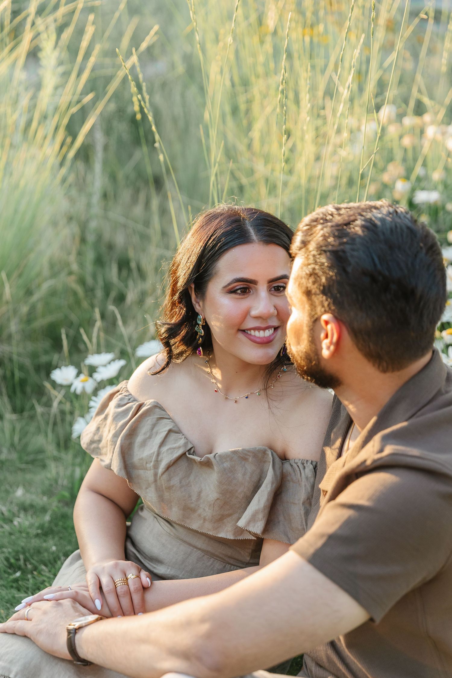 A romantic couple sits together in tall grass during a summer photo session.
