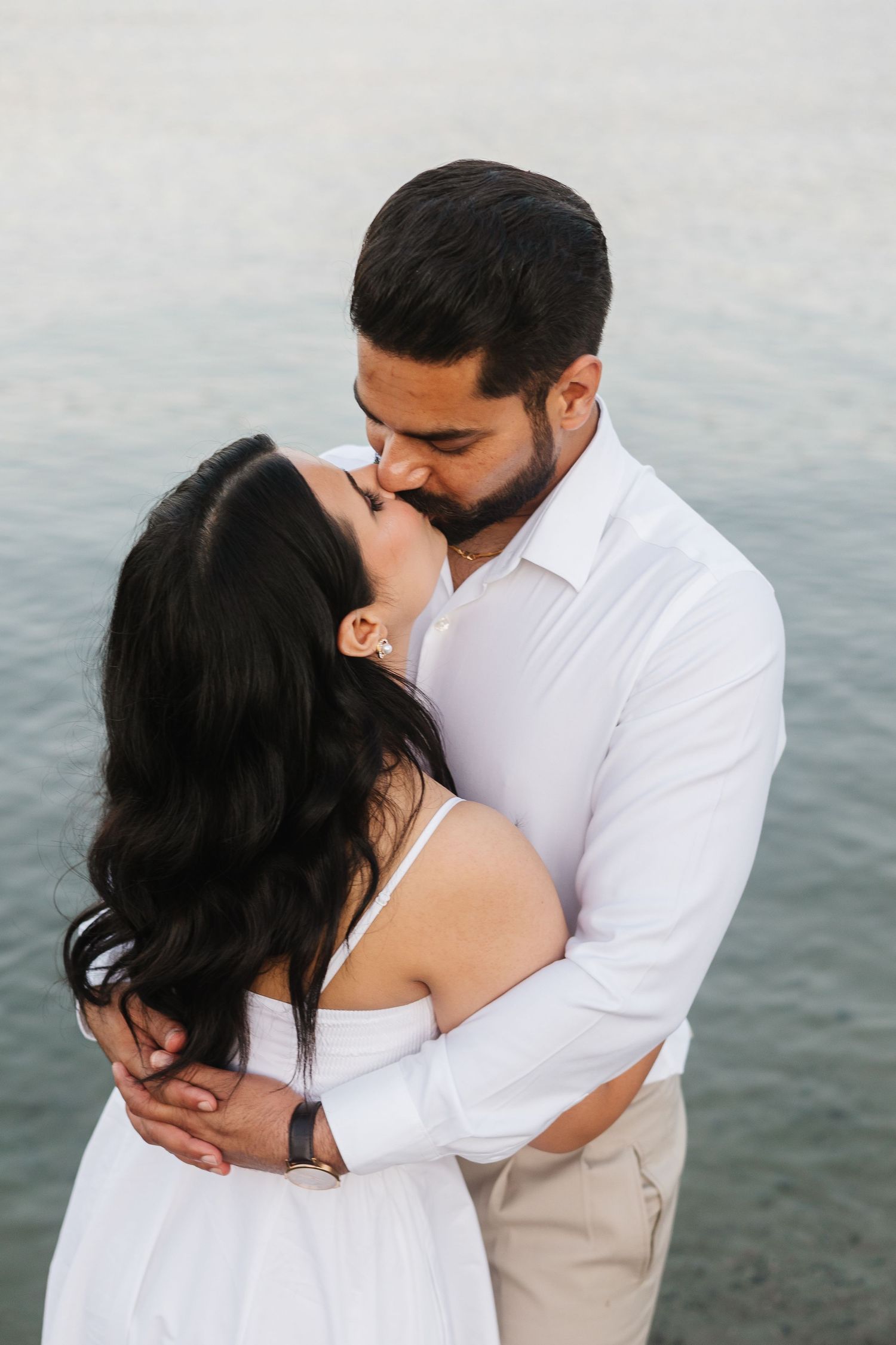 A romantic couple in white outfits sharing tender moments by the water in a series of intimate photographs.