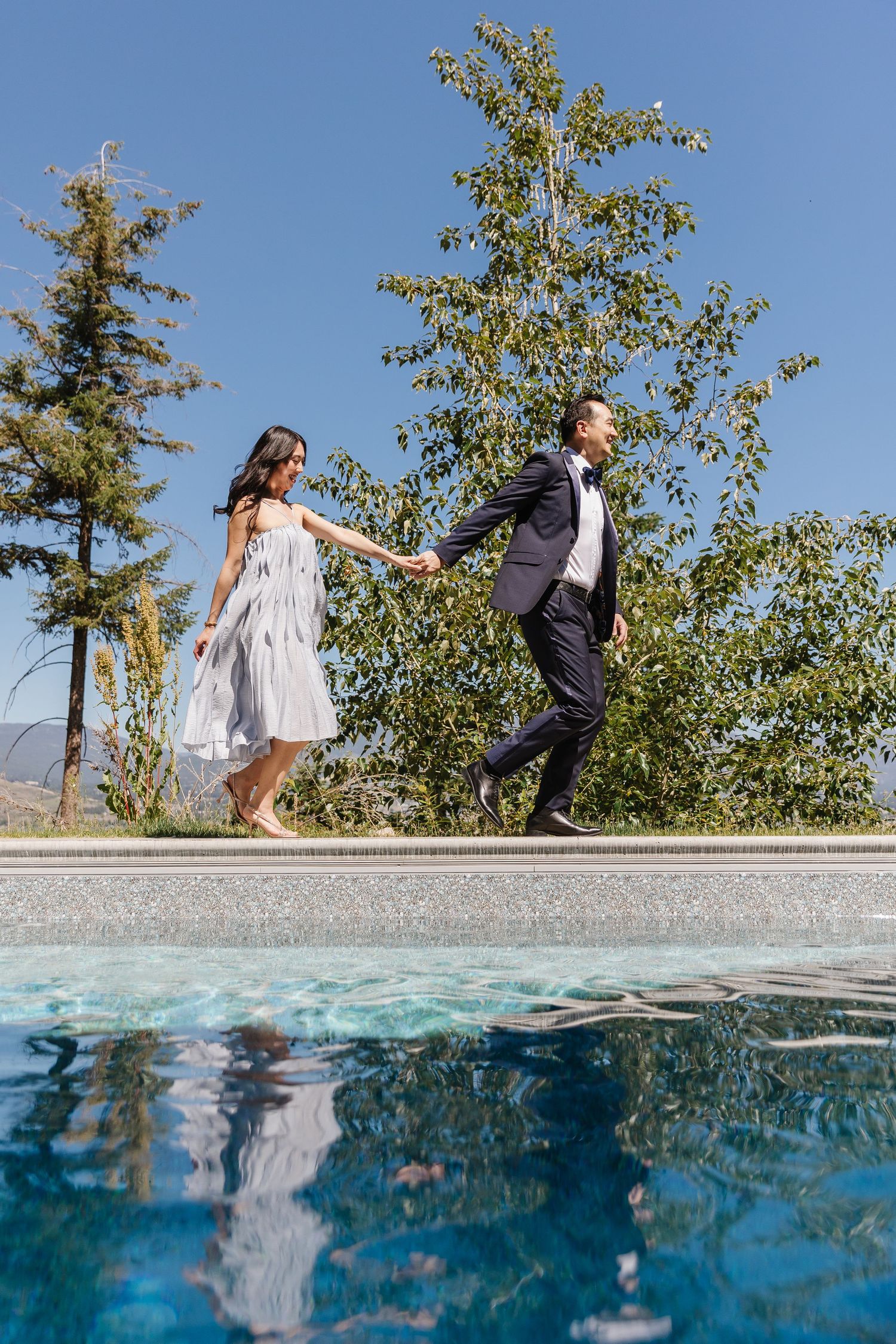 A couple playfully poses for split underwater and above water photos at the edge of a pool on a sunny day.