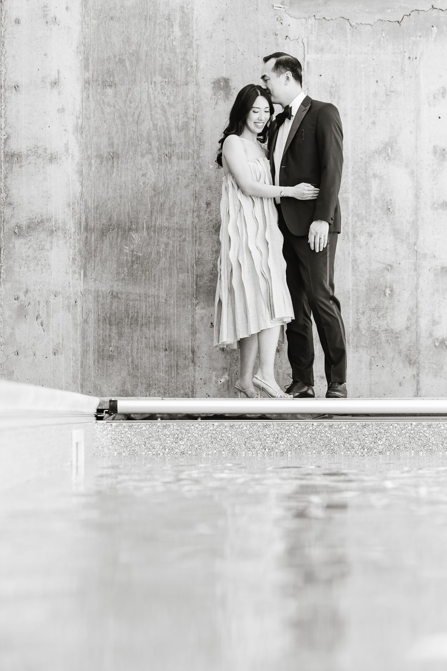 Black and white romantic engagement photos against a concrete wall show tender moments between a couple.