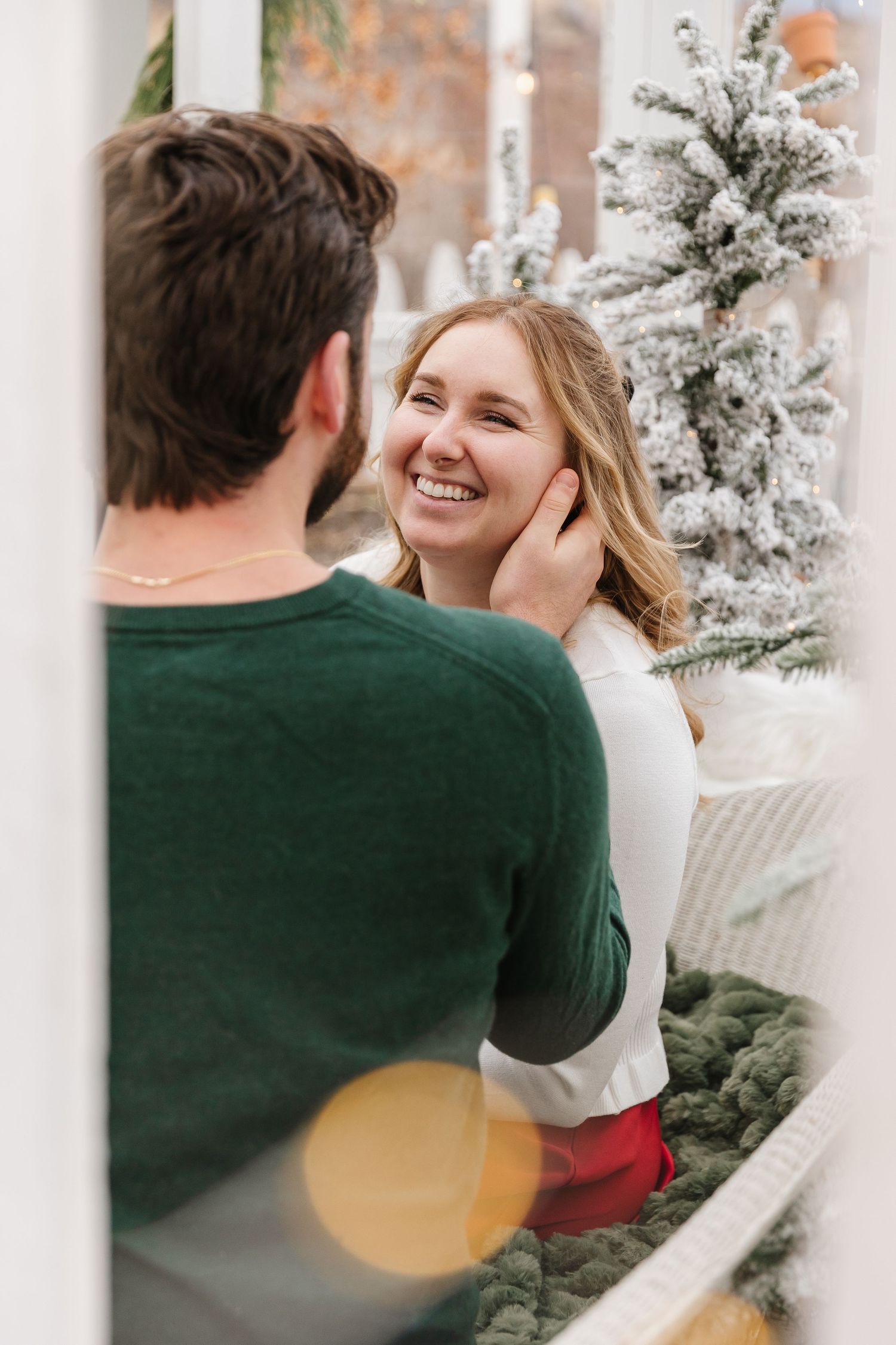 A couple shares a joyful moment together surrounded by snowy white Christmas trees in a winter holiday setting.