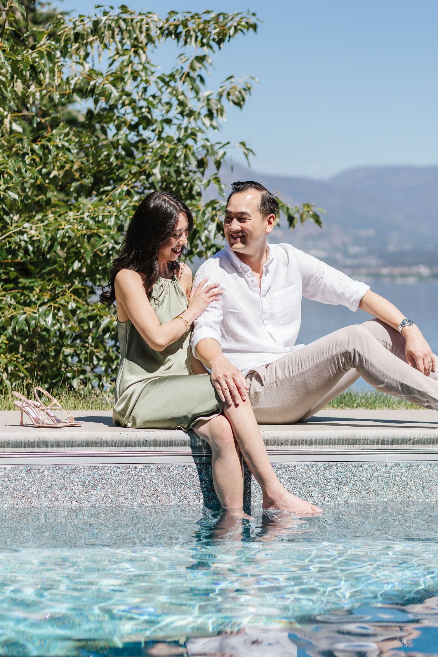 Couple relaxes and shares playful moments while sitting at the edge of an infinity pool with mountain views.