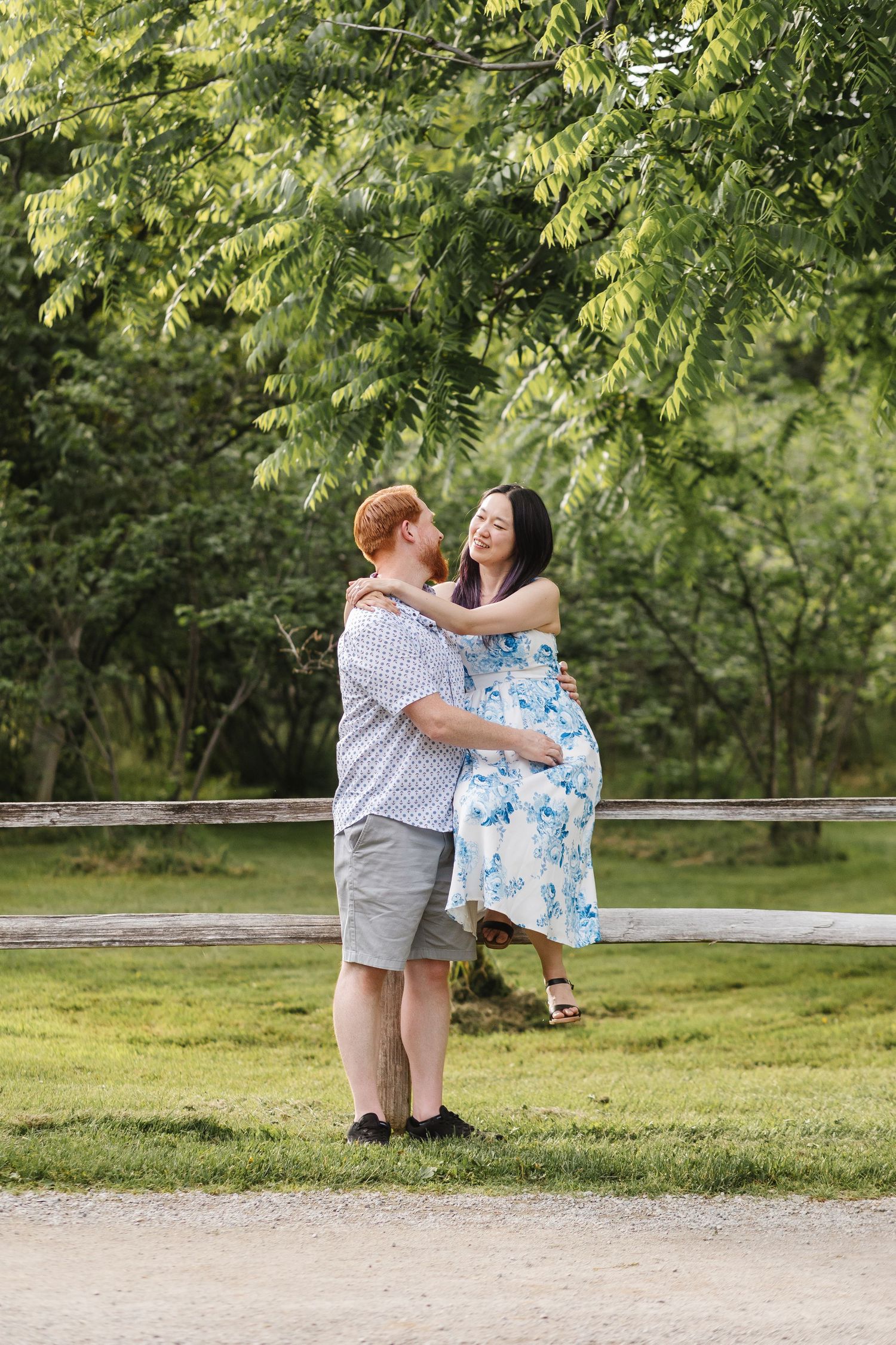 A couple shares a romantic moment embracing on a path under green trees in a park setting.