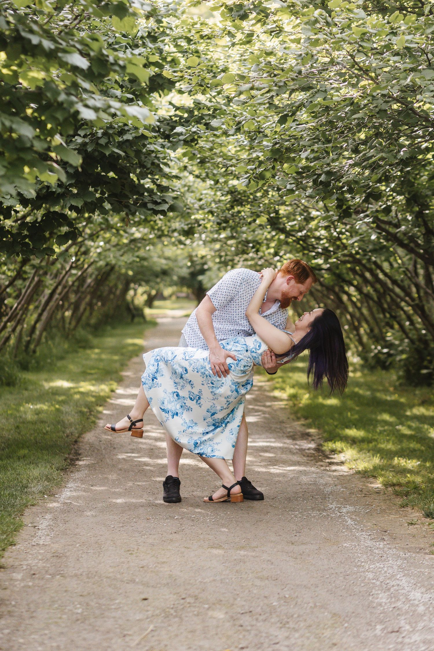 A romantic couple dances together on a garden path surrounded by lush green foliage on a summer day.