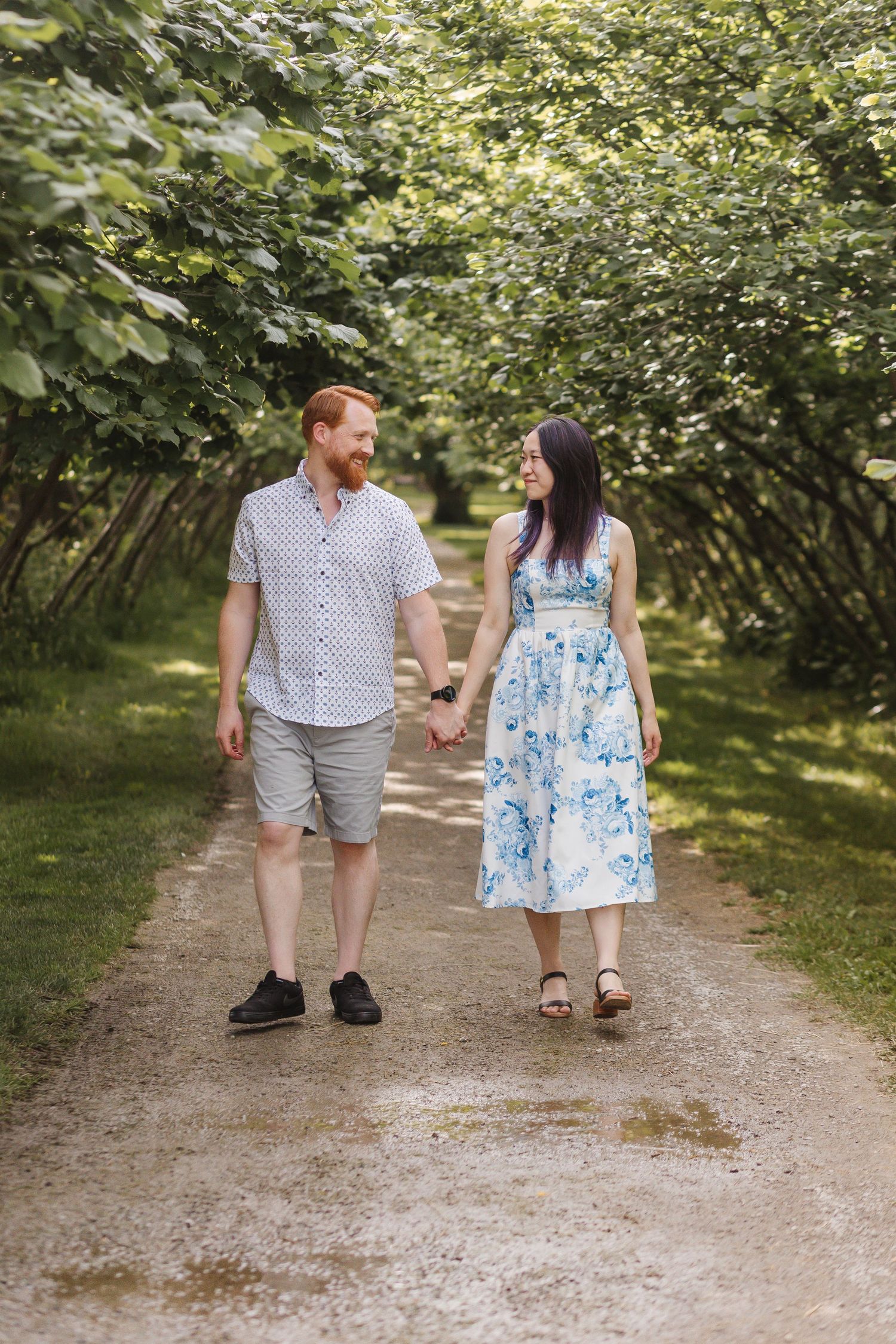 A couple walking hand in hand down a tree-lined gravel path on a sunny summer day.