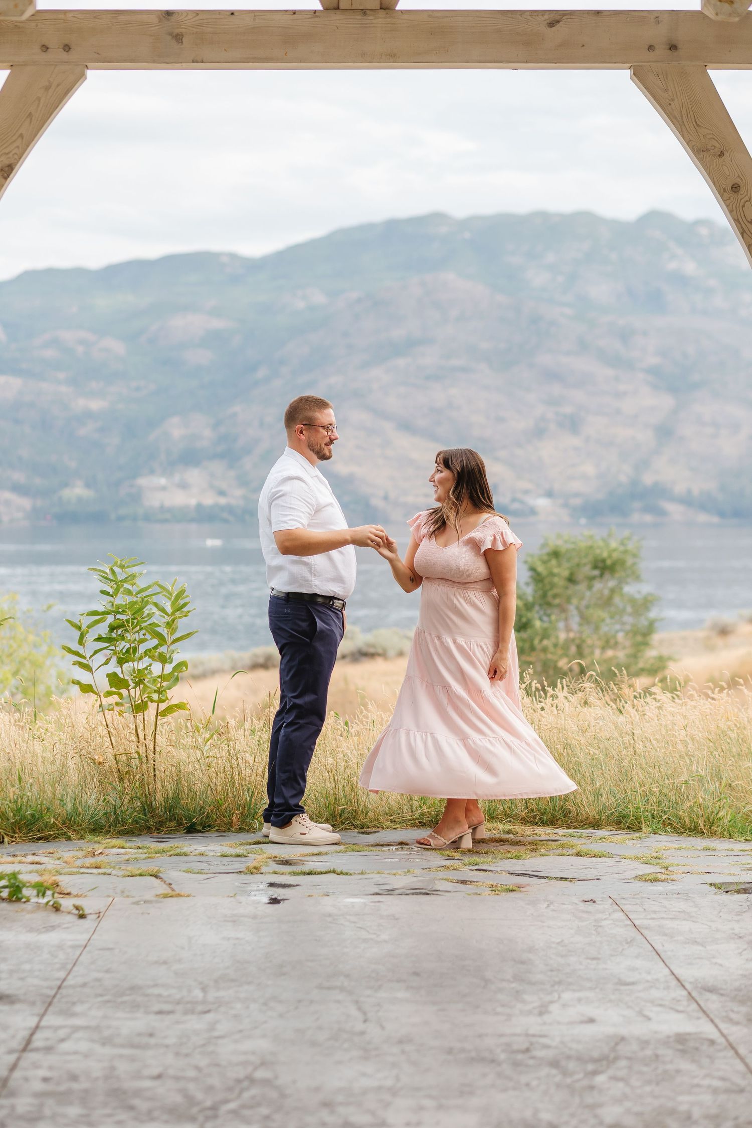 A couple dances together on a concrete platform with mountains and a lake in the scenic background.