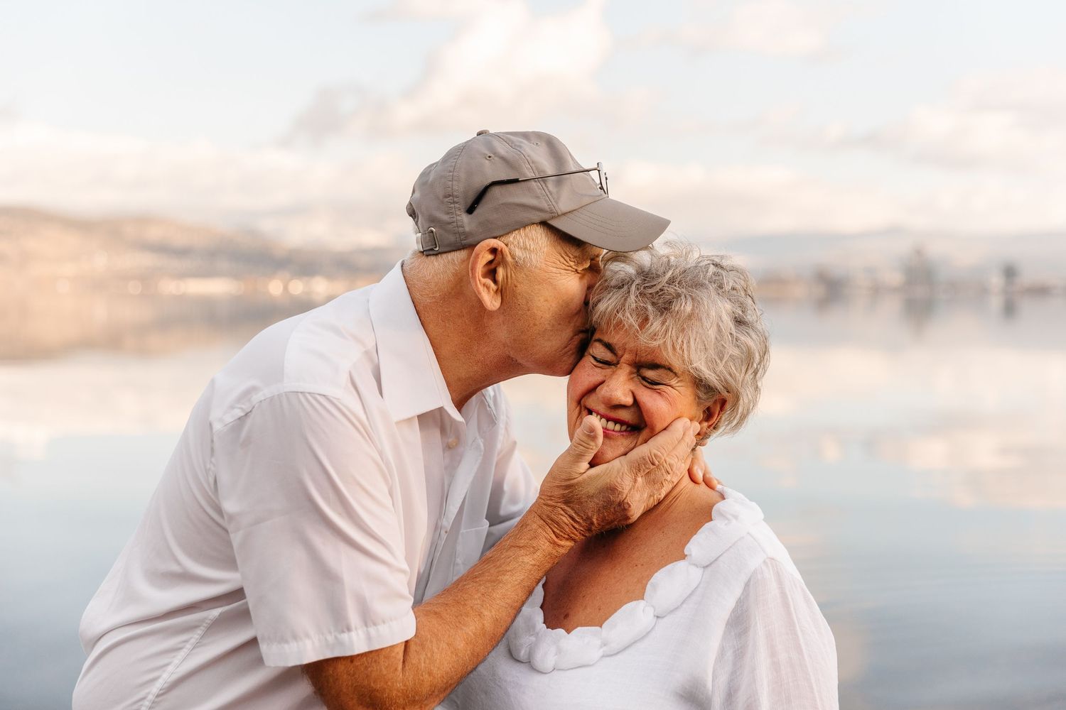 Senior couple sharing tender moment against serene waterfront backdrop.