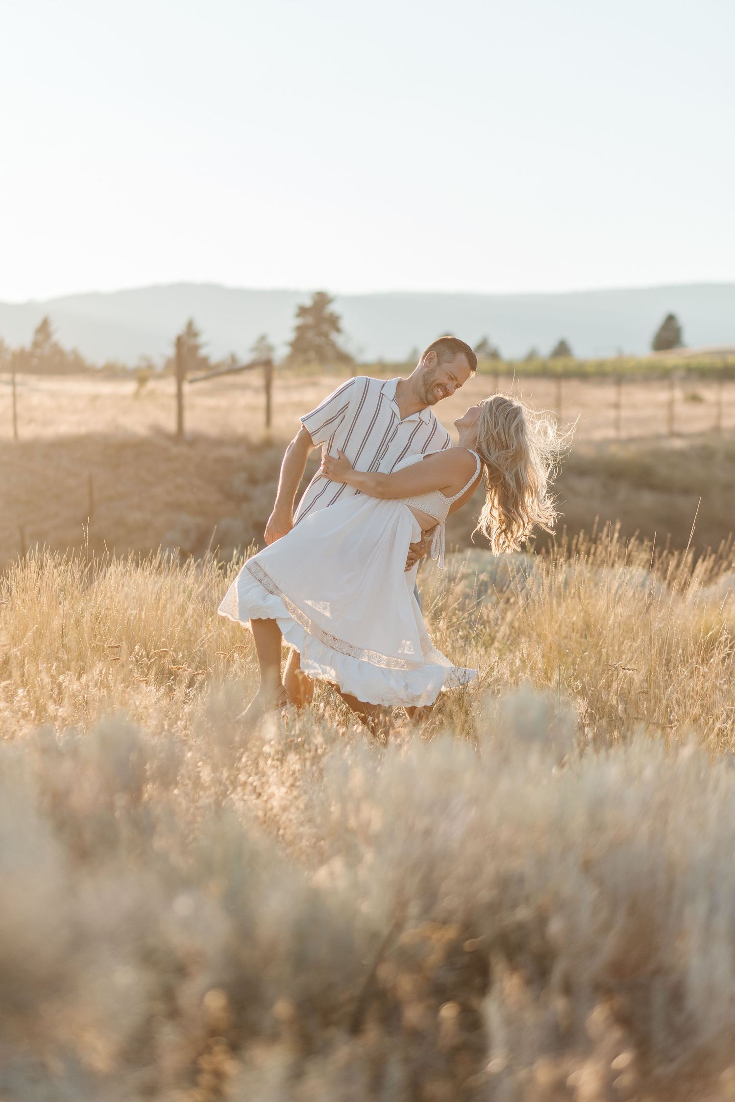 Romantic couple dancing and twirling in a sunlit field of tall golden grass during sunset.