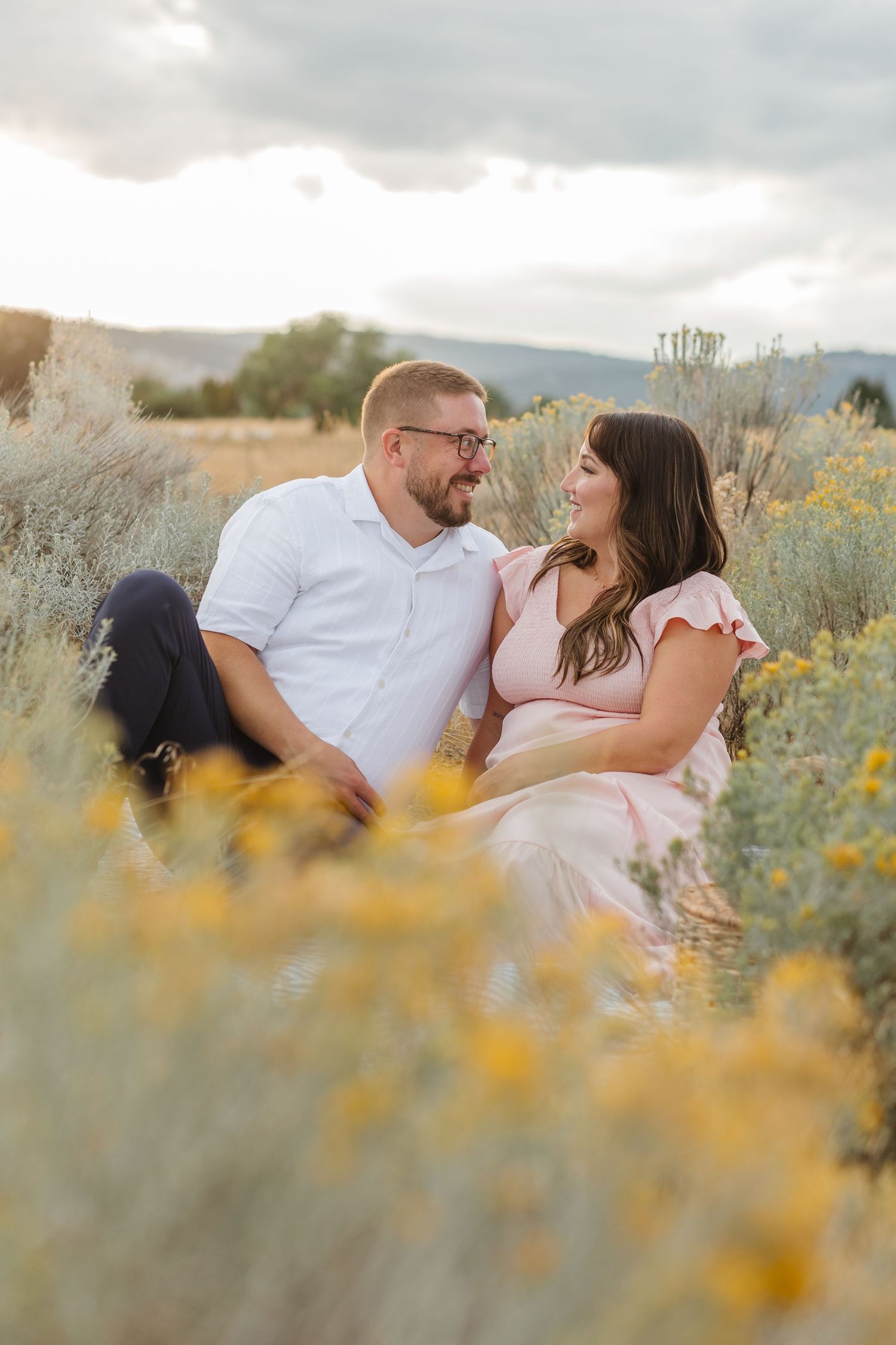 A couple lying together in a field of yellow wildflowers with mountains visible in the distance.