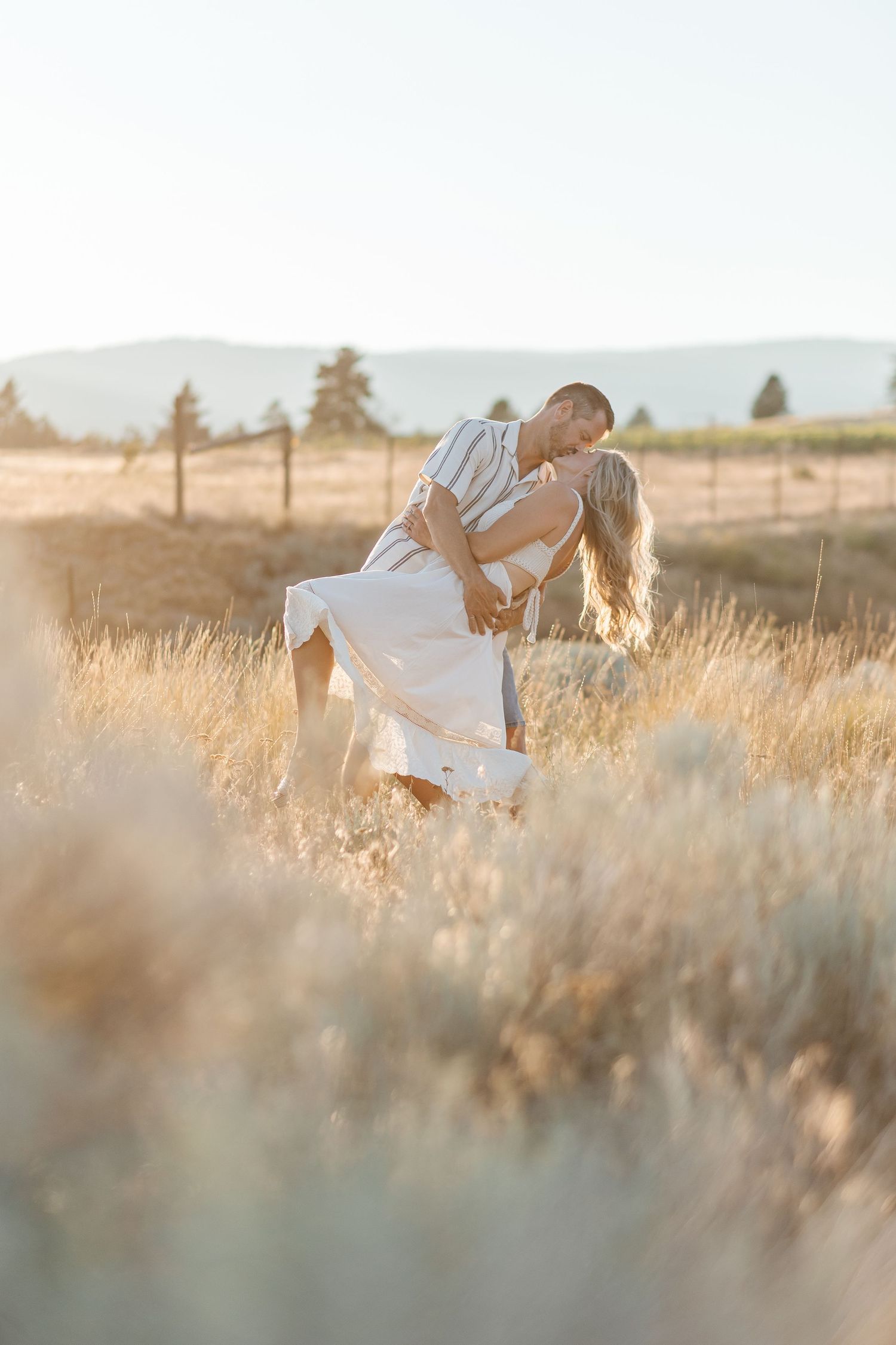 A white-dressed figure dances gracefully through a sun-lit field of tall golden grass at sunset.