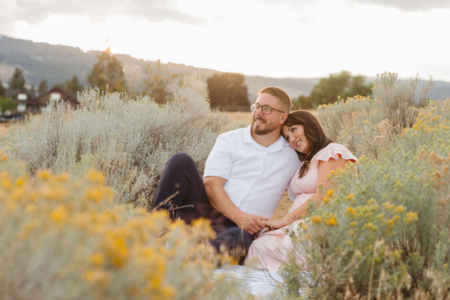 Couple sits together in a blooming yellow wildflower field during golden hour.