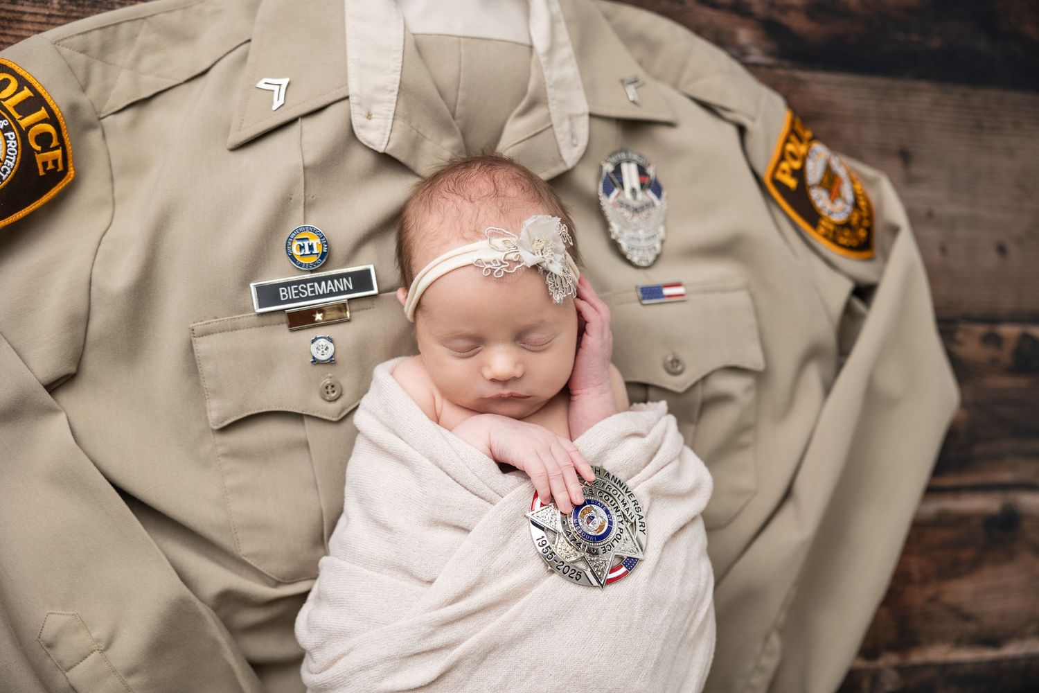 A newborn wrapped in white swaddle rests on a tan Scout uniform with various badges and patches against wood background.