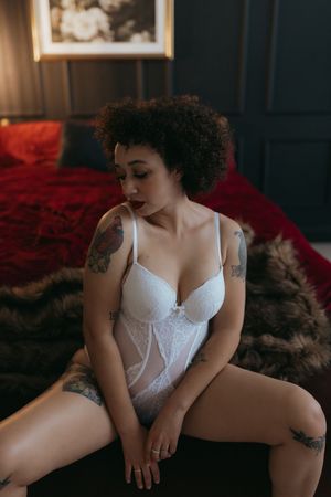 adult person sitting on a bench with fur, wearing light colored lingerie, posed with legs wide and looking down