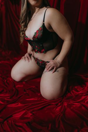adult person posing on a bed, wearing black  and red lingerie, during a boudoir photography session