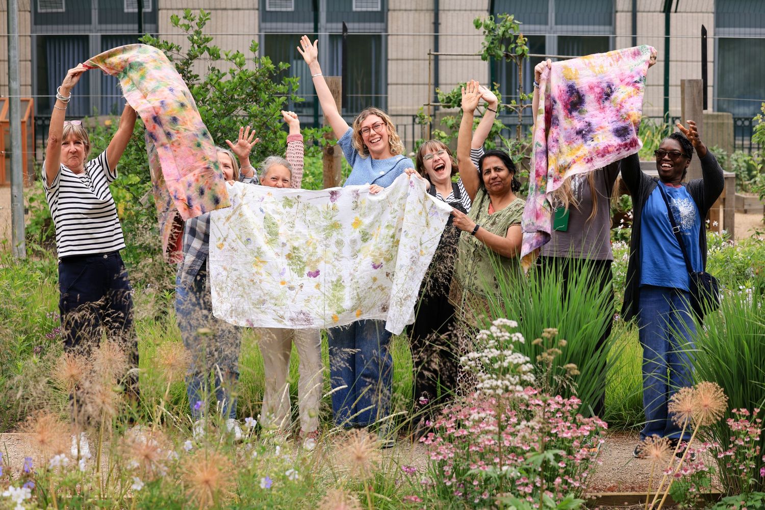 six women of different ages standing happy  waving naturally dyed textiles in a garden space