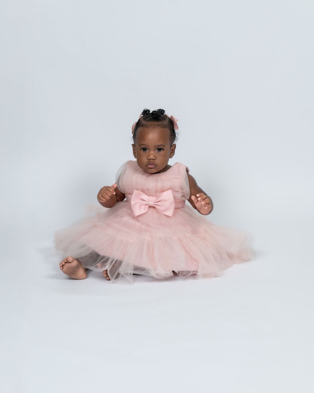 Baby girl in pink tulle bow dress sits on white background.