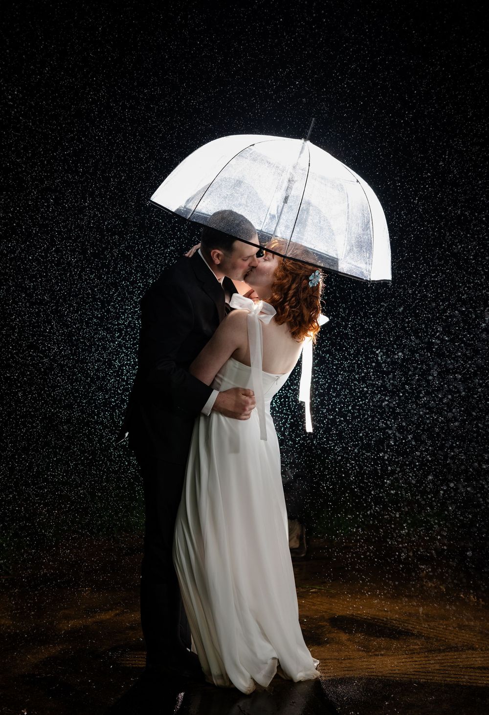 Bride and groom kissing under a clear umbrella in the rain at night at their White River wedding near Mountain Home, Arkansas