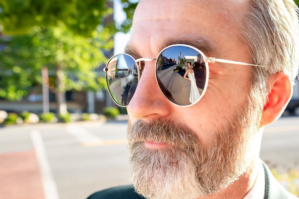 Close-up portrait of bearded man wearing reflective round sunglasses outdoors on sunny day.