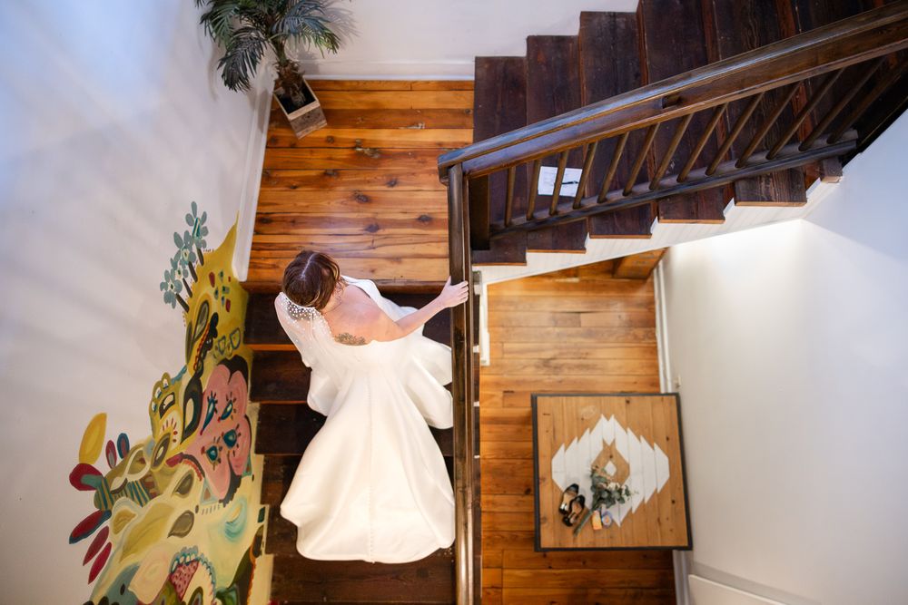 Bride descending a wooden staircase beside a colorful floral mural at a Northwest Arkansas wedding